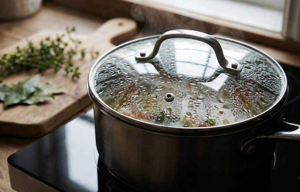 Une casserole mijotant avec un couvercle en verre couvert de condensation, illustrant l'astuce simple pour retenir la chaleur et économiser l'énergie.
