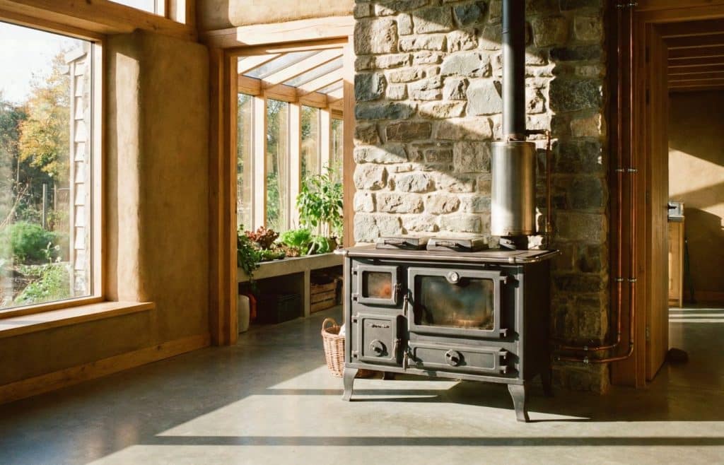 Cuisinière à bois bouilleur en fonte installée au cœur d'une maison bioclimatique lumineuse avec murs en pierre et matériaux écologiques.