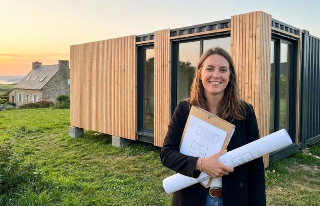 Elise Durant tenant les plans du permis de construire devant son extension de maison container avec bardage bois en Bretagne
