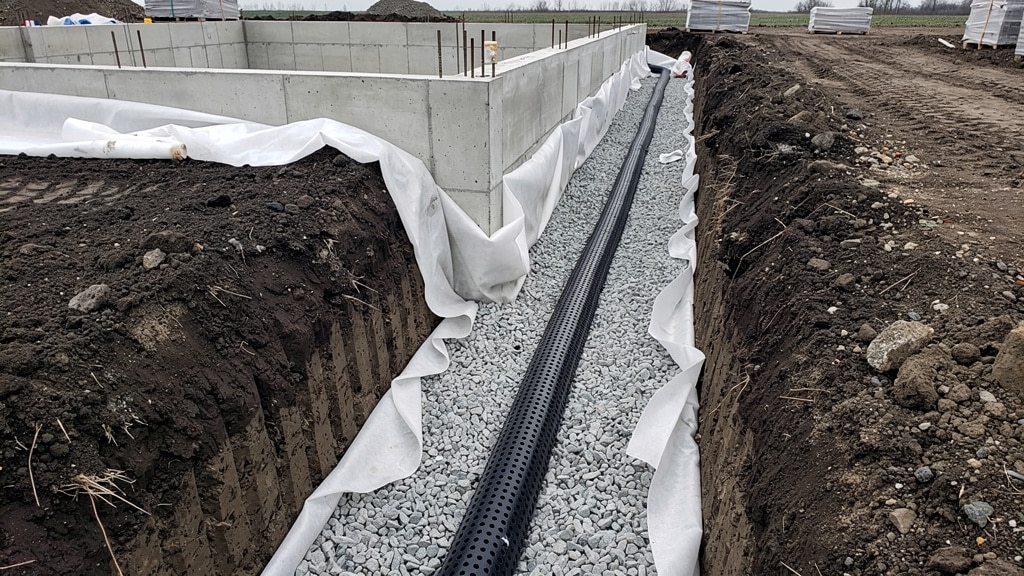 Drainage maison : drain crépiné posé sur graviers dans une tranchée le long des fondations