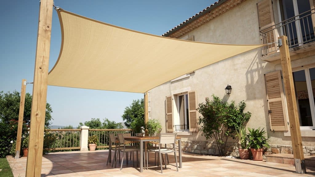 Voile d'ombrage beige tendue au-dessus d'une terrasse entre façade et mâts en bois