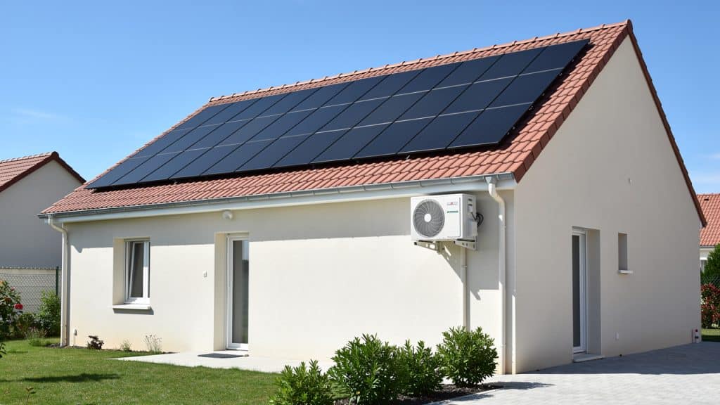 Panneaux solaires en toiture et unité extérieure de climatisation sur une maison individuelle