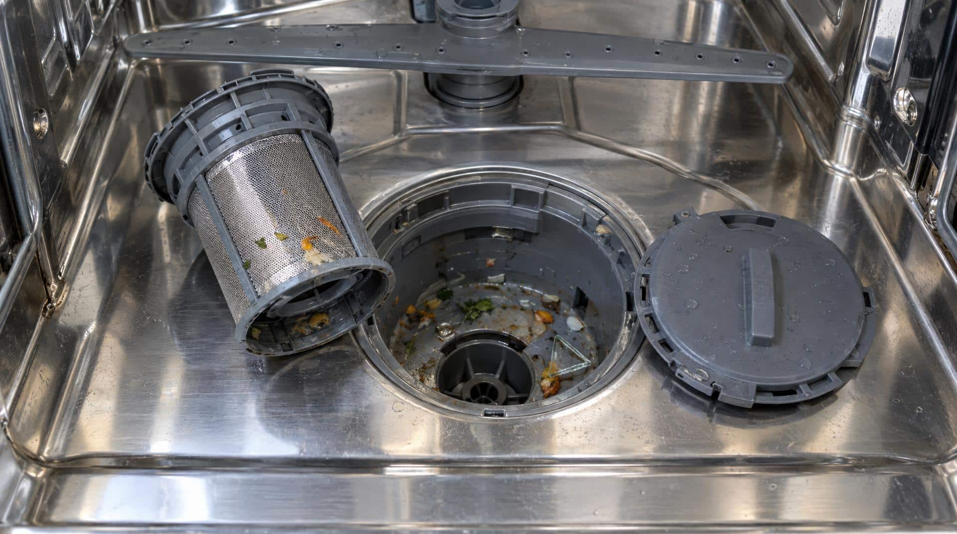 Fond de cuve d'un lave-vaisselle Bosch : filtre cylindrique sorti, couvercle de la pompe de vidange retiré et éclat de verre dans le puisard