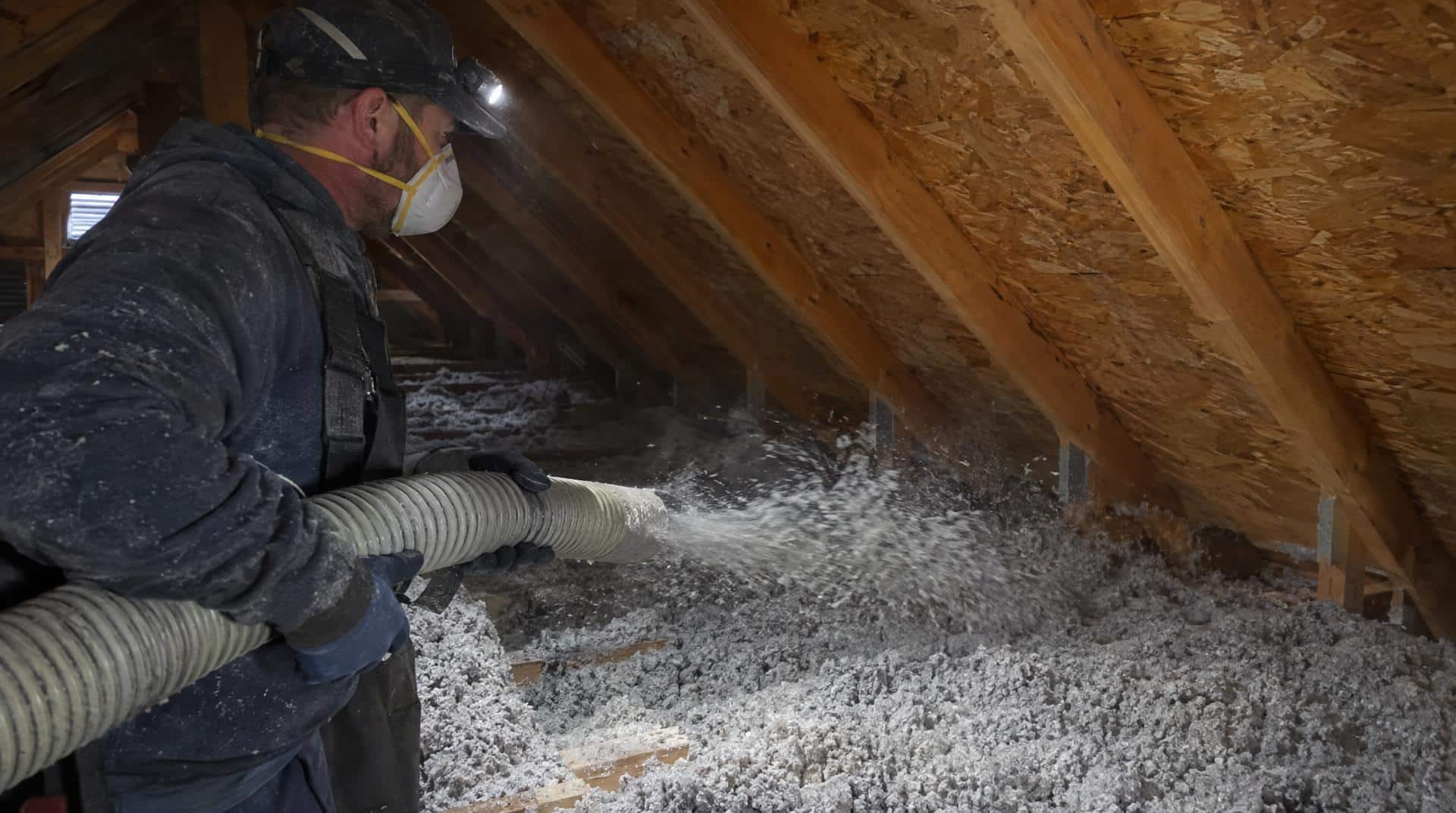 Artisan masqué soufflant de la ouate de cellulose en vrac dans des combles perdus