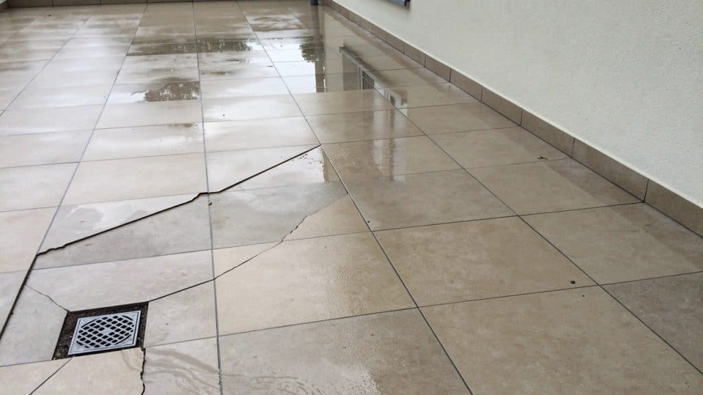 Étanchéité d’une terrasse carrelée : flaque d’eau stagnante et carreaux fissurés près d’une évacuation